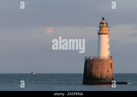 Ein Fischerboot vorbei an den Rattray Head Lighthouse am späten Nachmittag kurz nach Mondaufgang Stockfoto