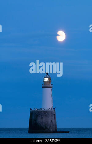 Rattray Head Lighthouse aus der nordöstlichen Küste von Schottland blinkt in der Dämmerung unter einem fast vollen Mond kurz nach Mondaufgang Stockfoto