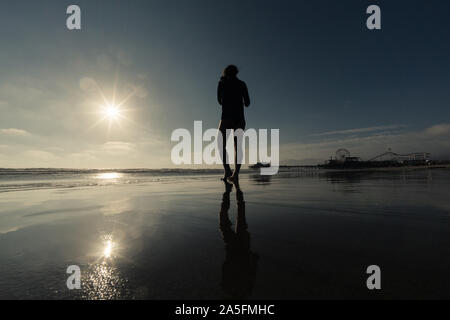 Silhouette einer Frau zu Fuß am Strand bei Sonnenuntergang, Santa Monica, California, United States Stockfoto