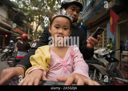 Hanoi, Vietnam - März 02, 2016: Vater mit Smartphone, und niedlichen Tochter mit Prinzessin Kostüm im Motorrad durch die Straßen von Hanoi Stockfoto