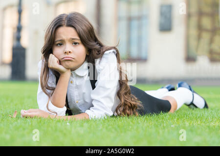 Traurig ohne ein Lächeln. Traurig Schulmädchen auf grünem Gras entspannen. Adorable kleine Kind mit traurigen Emotionen im Gesicht. Traurig und unglücklich. Traurigkeit und Depression. Schule Probleme. Stockfoto