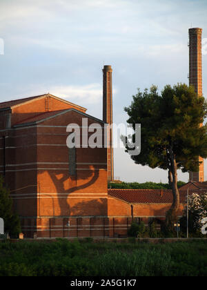 Schatten des grossen Baum auf der Giebelseite Wand der alten roten Ziegeln industrielle Gebäude am Ufer des Flusses Arno, Pisa, Italien Stockfoto
