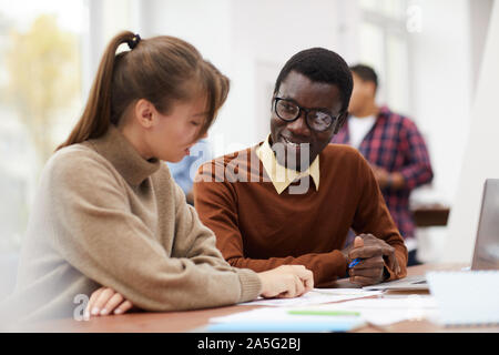 Portrait von lächelnden afroamerikanischen Schüler sitzen am Schreibtisch in der Hochschule und genießen Klasse mit weiblichen Mitschüler, kopieren Raum Stockfoto