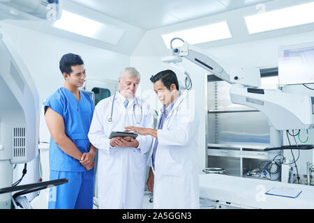 Ärzte und Chirurgen im Operationssaal zur Krankengeschichte des Patienten vor der Operation besprechen Stockfoto