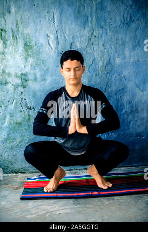 Teenager tragen schwarze Kleidung und Yoga auf farbenfrohen traditionellen Matte und berühmten girlande Pose oder malasana. Vertikale erschossen. Stockfoto