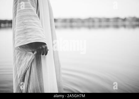 Nahaufnahme einer Person, die eine biblische Robe trug, während sie Stehen im Wasser in schwarz und weiß Stockfoto