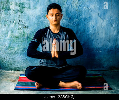 Einfache Pose oder sukhasana von einem jungen Mann auf der bunten Mat durch das Tragen schwarzer Kleidung durchgeführt. Stockfoto