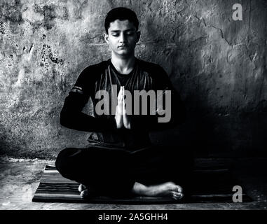 Einfache Pose oder sukhasana von einem jungen Mann auf der bunten Mat durch das Tragen schwarzer Kleidung durchgeführt. Stockfoto