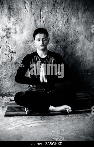 Einfache Pose oder sukhasana von einem jungen Mann auf der bunten Mat durch das Tragen schwarzer Kleidung durchgeführt. Stockfoto