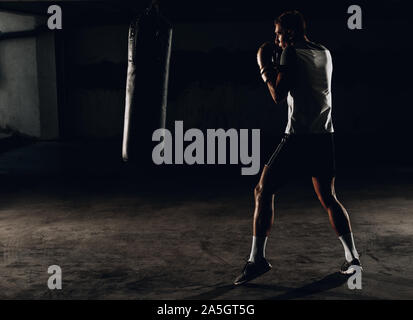 Junge Muskel Boxer mit einem Boxsack in der Turnhalle. Boxer schlagen Stanzgeschwindigkeit Tasche Stockfoto