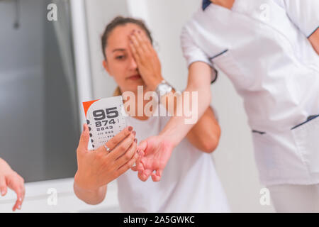 Frau (Mädchen) Überprüfung des Sehvermögens schließen Auge mit der Hand. Auge Test. Sehkraft Vision exam Chart. In der Nähe auf einem Snellen char Stockfoto