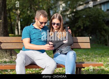 Schöne junge Paar auf der Bank sitzen im Park mit Handy Stockfoto
