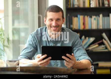 Vorderansicht Portrait eines glücklichen Mann hält Tablet an der Kamera in ein Café oder nach Hause sitzen auf der Suche Stockfoto