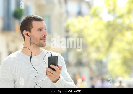 Schwere erwachsenen Mann tragen Kopfhörer suchen an der Seite Musikhören von smart phone auf der Straße Stockfoto