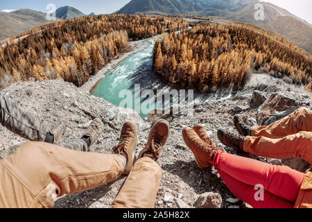 Vier Freunde sitzt und schaut auf Fluss und Berge. Schließen Sie herauf Foto der Beine Stockfoto