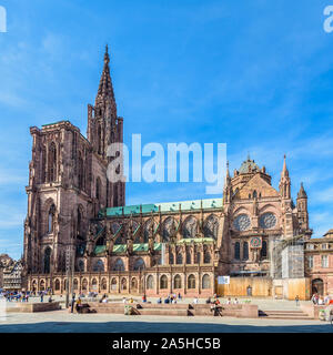 Der Turm und die Südseite der Kathedrale Notre-Dame in Straßburg, Frankreich, an einem sonnigen Tag mit Menschen bummeln und entspannen auf der Place du Chateau. Stockfoto