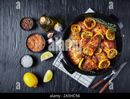 Hähnchen Schenkel mit gerösteten Zitronenscheiben und Thymian in eine schwarze Keramik Teller auf einem Holztisch, horizontale Ansicht von oben, flatlay, Kopieren spac Stockfoto