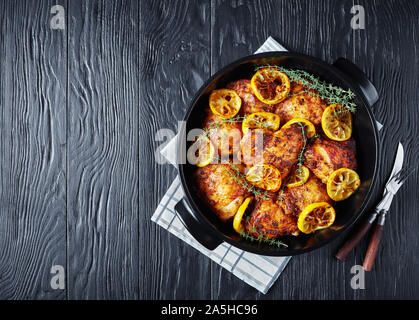 Hähnchen Schenkel mit gerösteten Zitronenscheiben und Thymian in eine schwarze Keramik Teller auf einem Holztisch, horizontale Ansicht von oben, flatlay, kostenfreie spac Stockfoto