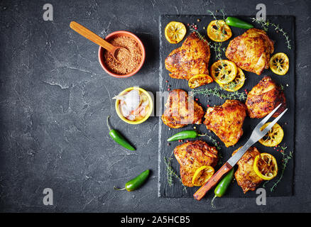 Knusprig gebratene Hühnerkeule mit gerösteten Zitronenscheiben und Thymian auf einen schwarzen Stein Board auf einer konkreten Tabelle, Ansicht von oben, flatlay, Nahaufnahme, freien s Stockfoto