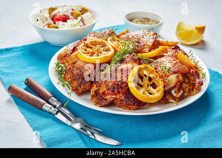 Knusprig gebratene saftige Hühnerkeule mit gerösteten Zitronenscheiben auf einer weißen Platte auf einer konkreten Tabelle mit Mediterraner Salat in eine Schüssel, Ansicht von oben Stockfoto