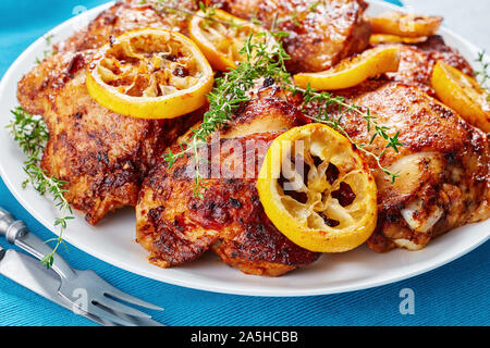 Nahaufnahme der knusprig gebratene saftige Hühnerkeule mit gerösteten Zitronenscheiben auf einer weißen Platte auf einer konkreten Tabelle mit griechischen Salat in eine Schüssel, Ansicht von Abo Stockfoto