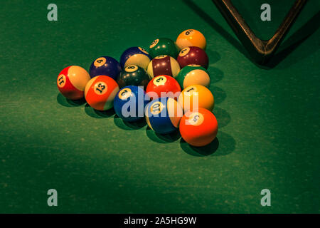 Set aus bunten Nummern auf den Kugeln am grünen Tisch und teilweise sichtbar Holz- Dreieck. Horizontale Hintergrund mit Ausrüstung für Americal Billardqueue Sport Stockfoto