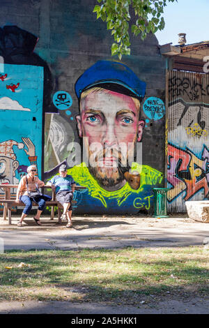 Ein rentnerehepaar sitzen entspannt auf einer Bank vor einer Wand Kunst Portrait - grafittee, Redon, Frankreich Stockfoto