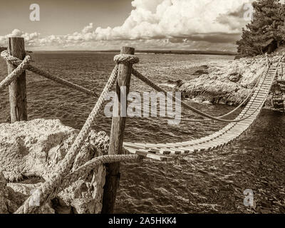 Hängende Holzbrücke felsigen Küste verbinden, Sepia Stockfoto