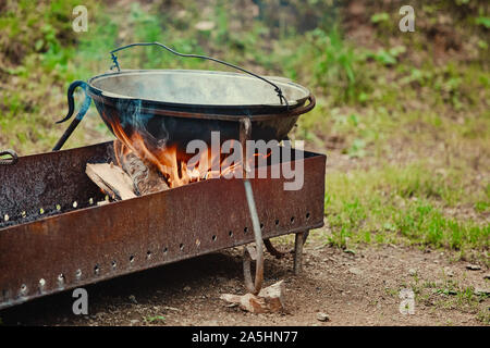 Ein metall Kessel steht auf einem Grill mit Feuer und Brennholz, in einem touristischen Parkplatz. Stockfoto