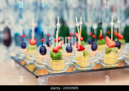 Obst Häppchen auf einem Glas Tablett, auf dem Hintergrund der Weingläser und Champagner. Catering Konzept. Stockfoto