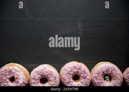 Oben Aufnahme einer schwarzen Holzfläche mit rosa Donuts Auf der Unterseite Stockfoto