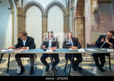 21. Oktober 2019, Sachsen-Anhalt, Magdeburg: Harald Meller, (L - r), Archäologe, Sachsen-Anhalt, Gunnar Schellenberger, Staatssekretär für Kultur in Sachsen-Anhalt und Jonathan Williams, stellvertretender Direktor des British Museum unterzeichnen die Verträge für die Zusammenarbeit zwischen den Staatlichen Museum für Ur- und Frühgeschichte und das Britische Museum im Kunstmuseum Kloster Unser Lieben Frauen Magdeburg. Auf der rechten Seite, Neil Wilkin, Kuratorin für die Bronzezeit im Britischen Museum, Fotos der Prozess. Das Kooperationsabkommen zwischen den beiden Museen regelt künftige Darlehen zwischen den beiden Museen. Von 20 Novem Stockfoto