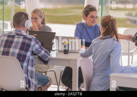 Die Menschen in der Cafeteria sitzen, während im Gespräch und mit Hilfe von Computern, während ein Mann mit einem Plaid Shirt Musik zu hören ist. Stockfoto