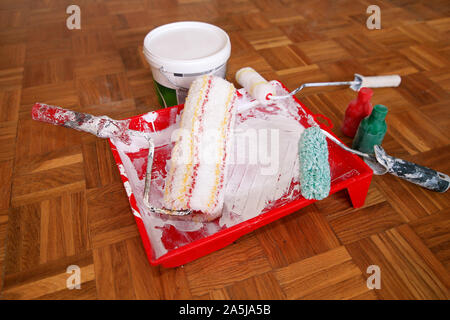 Wandmalerei, Geräte und Werkzeuge. Eimer mit weißer Farbe, rote und grüne Farbe Flasche, rot Schüssel für Farben-mischer und Wand Schrumpfung Farbroller Stockfoto