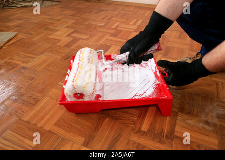 Bauarbeiter tun beenden Renovierung im Apartment. Maler mit Handschuhen hält weiße Walze Pinsel in der hand und Mixe Farbe in den Container. Stockfoto