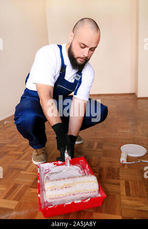 Bauarbeiter tun beenden Renovierung im Apartment. Maler mit Handschuhen hält weiße Walze Pinsel in der hand und Mixe Farbe in den Container. Stockfoto