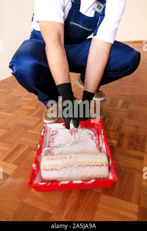 Bauarbeiter tun beenden Renovierung im Apartment. Maler mit Handschuhen hält weiße Walze Pinsel in der hand und Mixe Farbe in den Container. Stockfoto