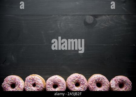 Oben Aufnahme einer schwarzen Holzfläche mit rosa Donuts Auf der Unterseite Stockfoto