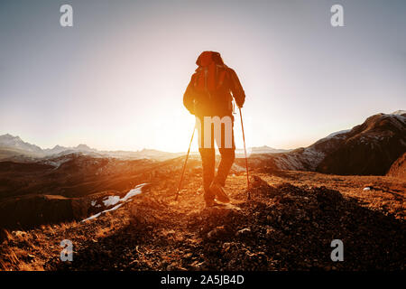 Silhouette der Wanderer mit Rucksack und Wanderstöcke geht in die Berge und den Sonnenuntergang Stockfoto