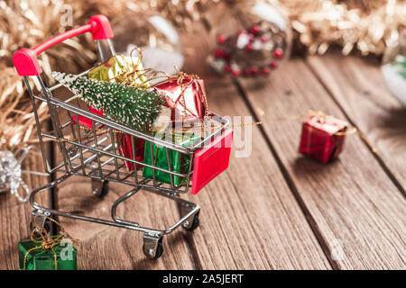 Shopping Cart mit Weihnachtsbaum und Miniatur Geschenk Boxen auf Holztisch. Weihnachten und Neujahr Shopping Konzept. Stockfoto