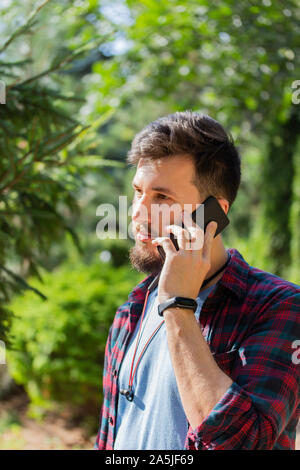 Hübscher junger brünett Mann mit einem Handy auf das Ohr. Portrait der kaukasischen Mann mit Bart und Schnurrbart, moderne Mode Frisur, kariertem Hemd, h Stockfoto