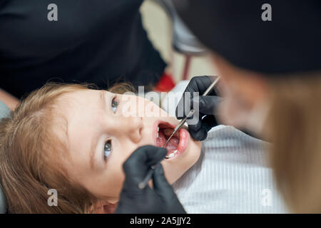 Nahaufnahme von kleinen Mädchen liegt am Behandlungsstuhl beim professionellen Zahnarzt in Schutzhandschuhe, Sonde und Härtung der Zähne. Patienten, die Zahnarztpraxis. Konzept der Pflege- und Verfahren. Stockfoto