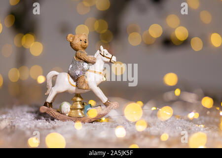 Dekorative Figuren aus einem Thema Weihnachten. Figur eines kleinen Teddybär auf einem Schaukelpferd. Weihnachtsdekoration. Festliches Dekor, warme Bokeh li Stockfoto