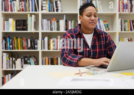 Portrait von lateinamerikanischen Frau mit Laptop während des Studiums in der Hochschule Bibliothek sitzen gegen Bücherregale, Kopie Raum Stockfoto