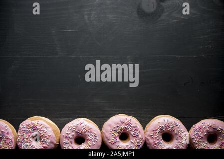 Oben Aufnahme einer schwarzen Holzfläche mit rosa Donuts Auf der Unterseite groß für Hintergrund Stockfoto