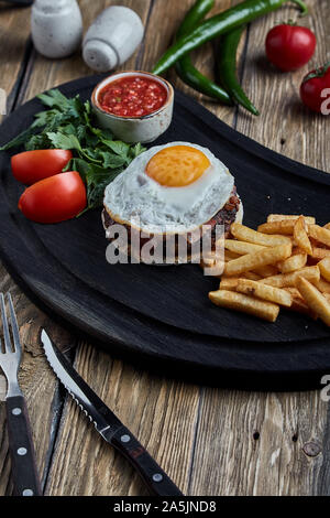 Rindersteak mit Ei und Salat aus grünen und Gemüse. Holz- Hintergrund, Tisch, feines Essen, Stockfoto