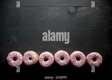 Oben Aufnahme einer schwarzen Holzfläche mit rosa Donuts Auf der Unterseite groß für Hintergrund Stockfoto