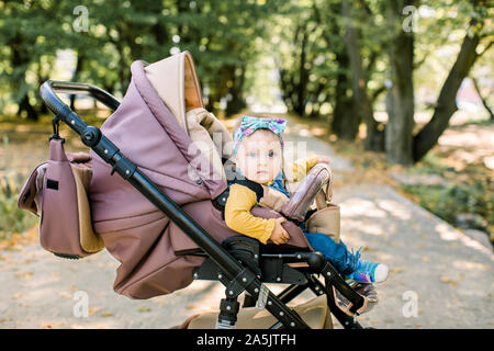 Süße kleine Baby Mädchen in Braun Kinderwagen im Park, abends Sonne Stockfoto