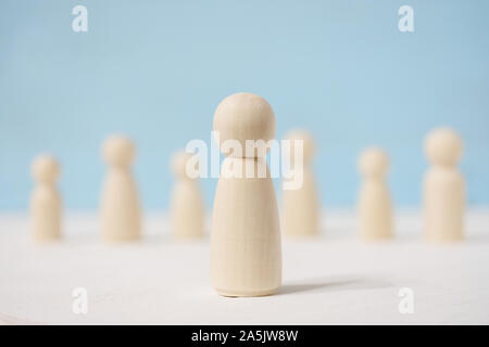 Abstrakte Holzfiguren von Mensch und Menschen unterscheiden sich von jeder anderen hinter ihm auf blauem Hintergrund. Konzept der Chef und Untergebenen. Stockfoto