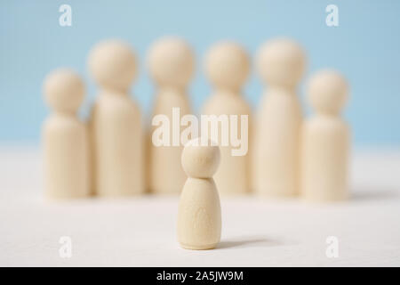 Abstrakte Holz- gesichtslose Figuren von Mensch und Menschen hinter ihm auf blauem Hintergrund. Konzept der Sprecher und Zuhörer, Chef und Untergebenen. Stockfoto